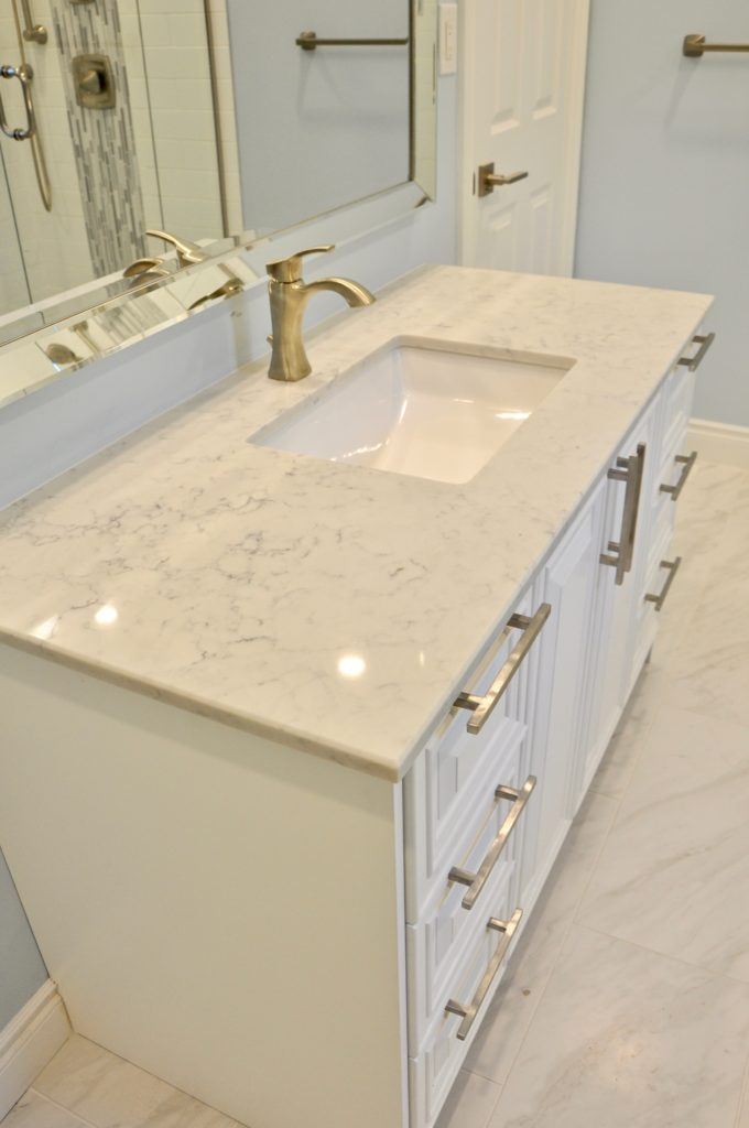 a white bathroom vanity with a white since and brass finishes